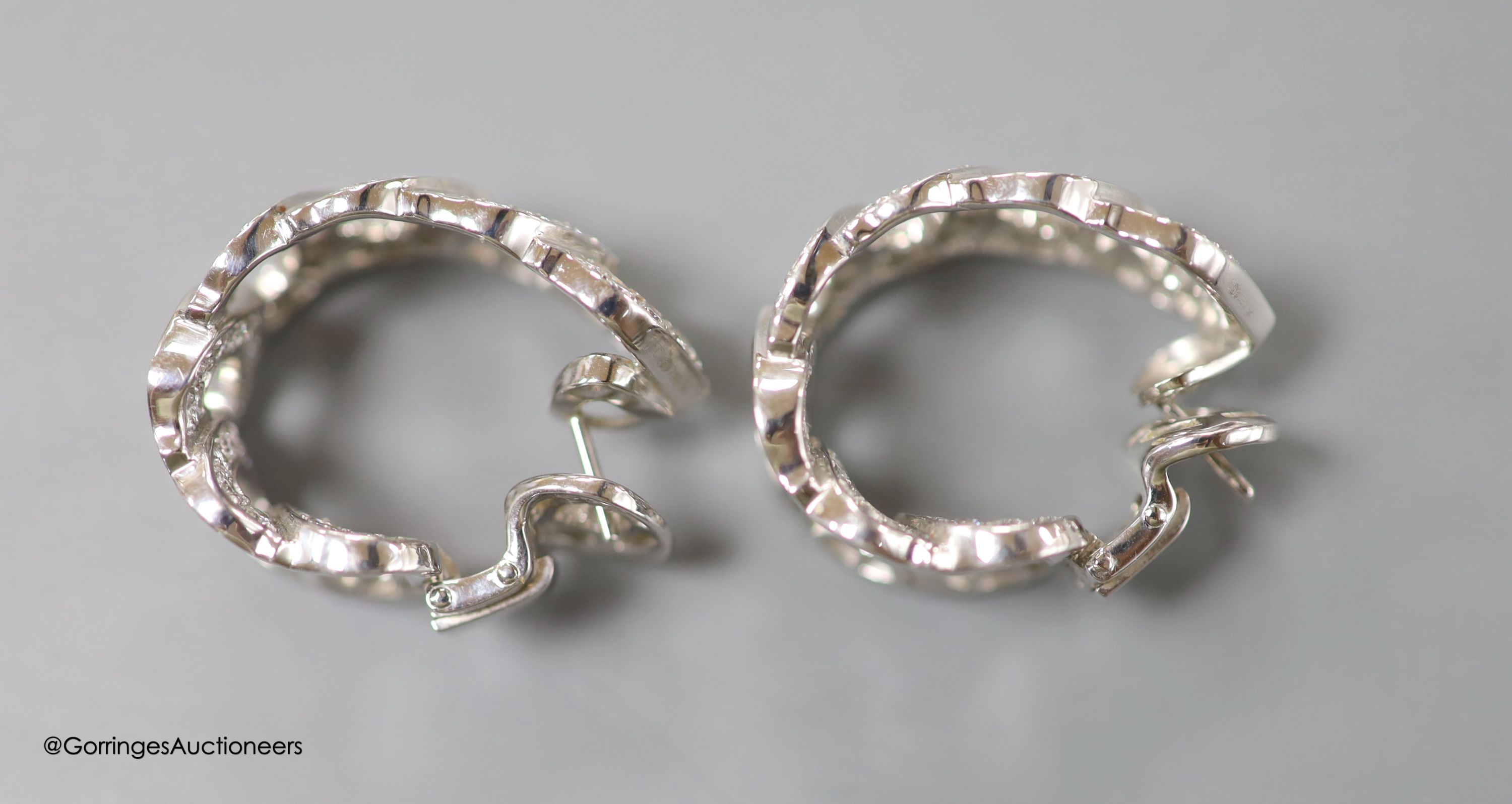 A modern pair of French Cartier white metal (18ct poincon mark) and diamond encrusted '7 C's' earrings, of curved form